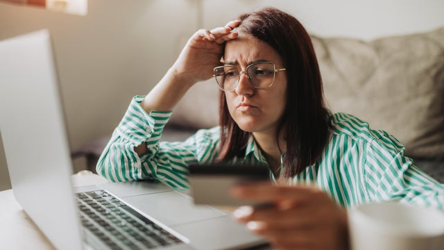 Young Worried Woman Shopping Online Holding Credit Card by a Laptop 