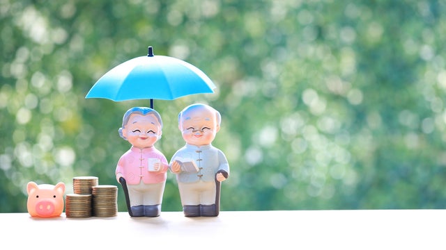 Senior couple figures under blue umbrella with stacks of coins on green background. Concept for retirement insurance, financial protection, elderly wealth management and pension security. 