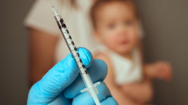 A parent holds a syringe ready for vaccination, focusing on the inoculation process. A child sits nearby, demonstrating a common healthcare practice and the importance of immunization 