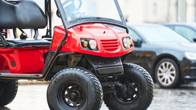 Red golf cart parked on city street on a rainy day 