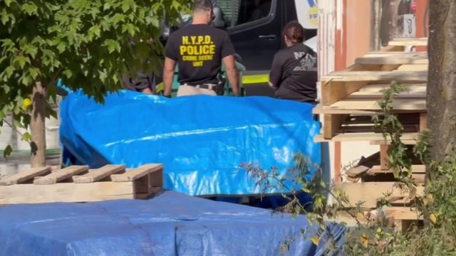 NYPD officials near a blue tarp apparently covering a body 